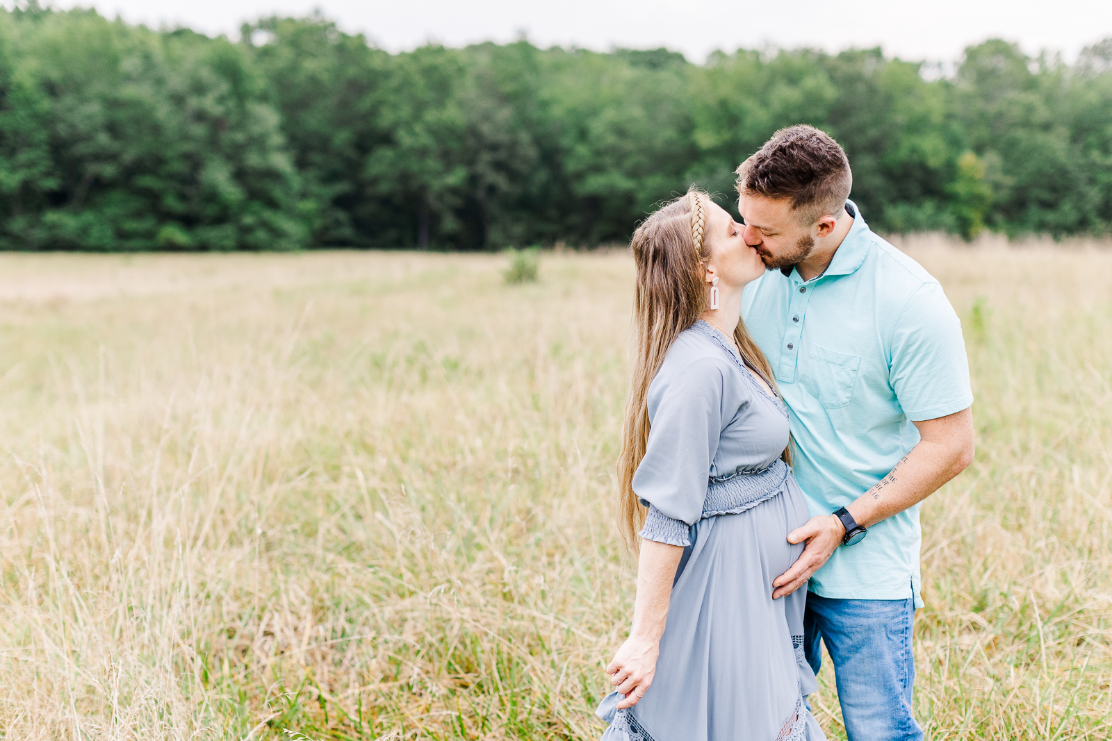 Pregnant mom-to-be kisses her husband as he holds his hand on her growing belly.